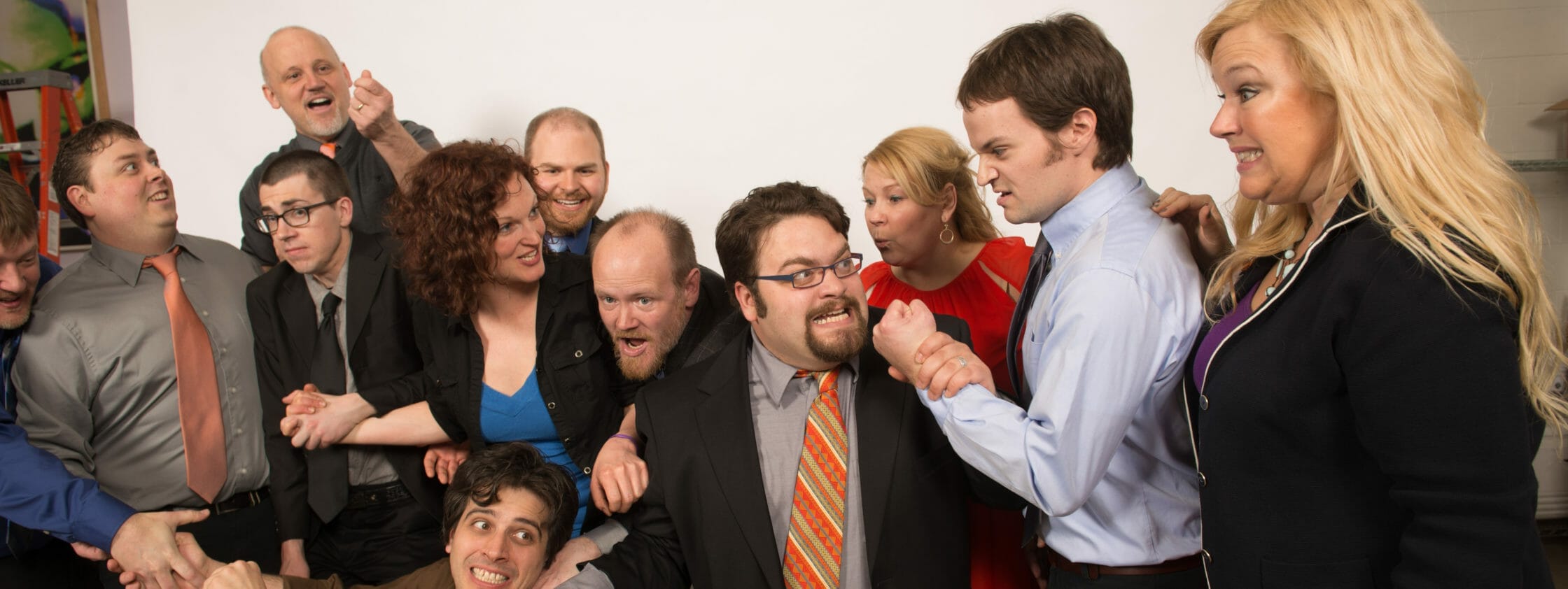 A lively group of people in formal attire, playfully engaging in a mock confrontation, showcasing a mix of expressions.