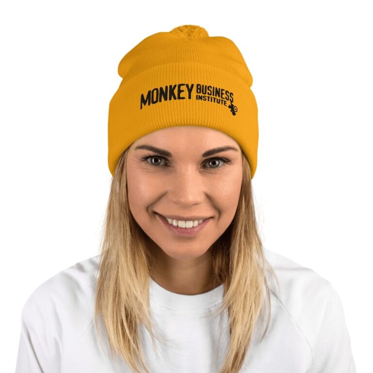 Smiling woman wearing a bright yellow beanie with "MONKEY BUSINESS INSTITUTE" printed on it, against a white background.