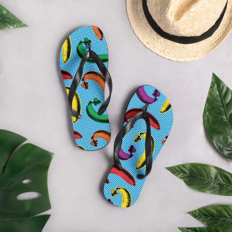 Colorful flip-flops with banana designs on a blue background, surrounded by tropical leaves and a straw hat.