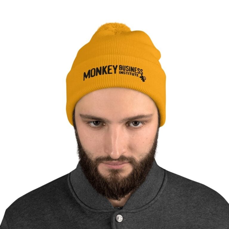 A man with a beard wears a bright yellow beanie featuring "Monkey Business Institute" in bold black text.