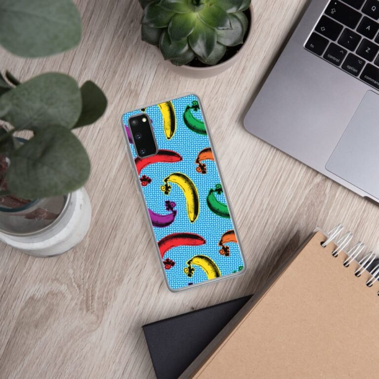 Colorful banana-patterned phone case on a wooden desk with plants, a laptop, and a notebook.